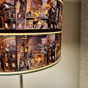 Pu&ograve; includere: Un paralume con un design di strisce di pellicola che mostrano un edificio scuro e in rovina con un bagliore giallo. L'edificio ha pi&ugrave; finestre e sembra essere in rovina.