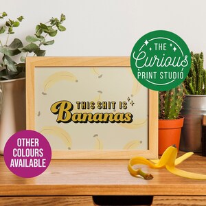 Puede incluir: Una impresión enmarcada con un patrón de plátanos amarillos y el texto "This Shit is Bananas" en una fuente retro. El marco es de madera clara y la impresión está rodeada por un borde blanco. La impresión es de The Curious Print Studio.