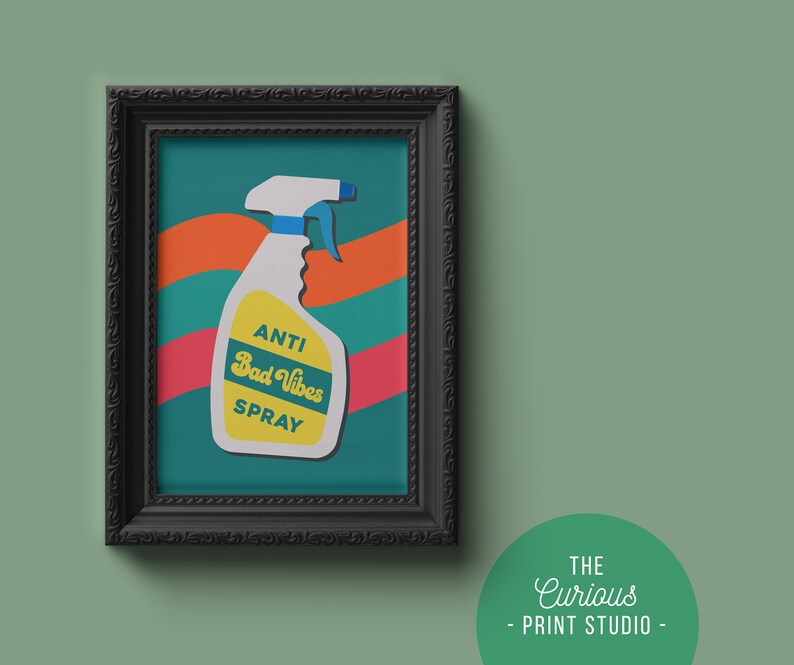 May include: A framed print featuring a colourful illustration of a spray bottle labelled "Anti Bad Vibes Spray". The background is teal green with orange and red wavy lines.