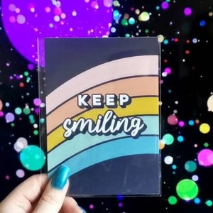May include: A colorful rainbow design with the text "KEEP smiling" on a black background. The design is printed on a clear card.