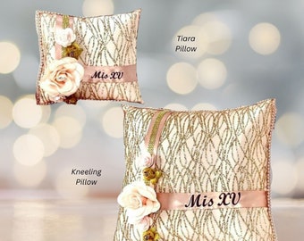 May include: Two decorative pillows with a gold and blush fabric. The larger pillow has a gold ribbon with the text "Mis XV" on it. The smaller pillow has a gold ribbon with the text "Mis XV" on it. Both pillows have a floral design.