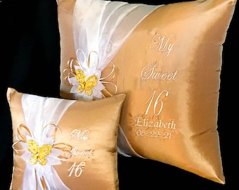 May include: Two gold and white satin pillows with embroidered text. The larger pillow reads "My Sweet 16 Elizabeth 05-22-21". The smaller pillow reads "My Sweet 16". Both pillows have a white sheer fabric overlay with a gold butterfly embellishment.
