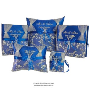 May include: A set of five blue and silver satin pillow boxes with embroidered text that reads "Mis 15 Años" and a name. The boxes are decorated with silver lace and blue ribbon.