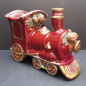 May include: A decorative ceramic train figurine in a vibrant red hue, accented with gold trim. The train features detailed wheels, a smokestack, and decorative floral elements. This collectible item is a charming addition to any home decor.