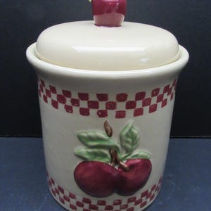 Puede incluir: Bote de cerámica color crema con tapa, con un patrón de cuadros rojos y blancos y un diseño de manzana en relieve. La tapa está rematada con un pequeño pomo en forma de manzana roja. Contenedor decorativo de cocina.