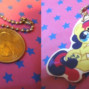 May include: Two My Little Pony keychains. One is green and blue, the other is yellow, red, and blue. Each keychain is attached to a silver ball chain. A U.S. quarter is next to each keychain for size comparison.