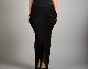 May include: A woman wearing a black sleeveless top and a long black skirt with a slit in the front. The skirt has a gathered, draped design.