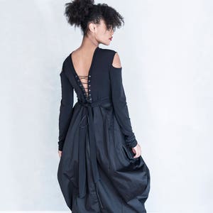 Pu&ograve; includere: Un abito nero a maniche lunghe con aperture sulle spalle, scollo a V profondo con chiusura a lacci stile corsetto sulla schiena e una gonna voluminosa e arricciata di lunghezza midi, abbinato a d&eacute;collet&eacute; nere con tacco alto.
