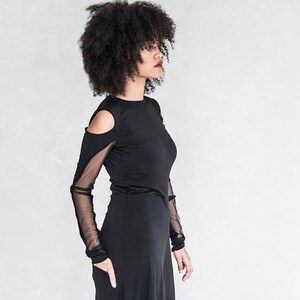 May include: A woman wearing a black maxi dress with sheer mesh sleeves and a cut-out detail at the shoulders.
