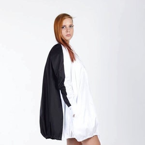 K&ouml;nnte beinhalten: Ein farblich abgesetztes Kleid mit einer einfarbig wei&szlig;en Vorderseite und einer einfarbig schwarzen R&uuml;ckseite. Das Kleidungsst&uuml;ck hat lange &Auml;rmel, einen abgerundeten Saum mit elastischem Abschluss und eine lockere, flie&szlig;ende Passform bis &uuml;ber das Knie.