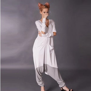 May include: A white jumpsuit with long sleeves and a V-neck. The jumpsuit has a gray panel at the bottom and is styled with black high heels.