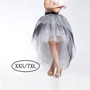 Può includere: Una gonna di tulle alta-bassa con un designo sfumato in bianco e nero. La gonna è a strati e ha un lungo strascico sul retro. La modella indossa la gonna con un boa di piume bianche e tacchi neri. Il testo "XXS/7XL" è visibile nell'immagine.