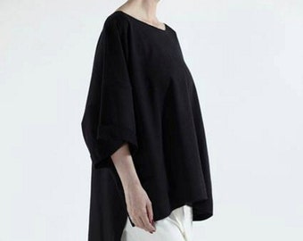 May include: A black, long-sleeved, loose-fitting shirt with a high, round neckline. The shirt is worn with white cropped pants and black sneakers.