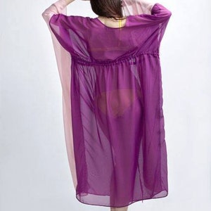 Puede incluir: Un vestido transparente de estilo caft&aacute;n morado y rosa. El vestido tiene cintura con cord&oacute;n y mangas anchas. La modelo lleva sandalias doradas. El vestido est&aacute; hecho de una tela ligera y fluida.