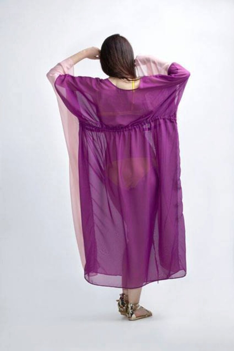 Puede incluir: Un vestido transparente de estilo caft&aacute;n morado y rosa. El vestido tiene cintura con cord&oacute;n y mangas anchas. La modelo lleva sandalias doradas. El vestido est&aacute; hecho de una tela ligera y fluida.