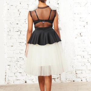 May include: A black sleeveless top featuring sheer mesh panels and white ruffled shoulder accents, paired with a black peplum waist and a layered white tulle skirt that falls to the knees, worn with black high-heeled shoes.