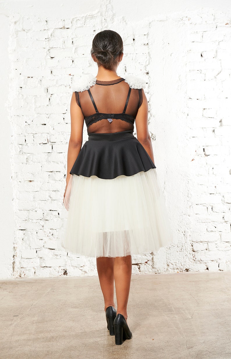May include: A black sleeveless top featuring sheer mesh panels and white ruffled shoulder accents, paired with a black peplum waist and a layered white tulle skirt that falls to the knees, worn with black high-heeled shoes.