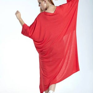 May include: A loose-fitting, vibrant red dress featuring a wide, rounded neckline and long, flowing batwing sleeves. The garment has a relaxed, oversized silhouette that drapes down to the lower calf, paired with white athletic sneakers.