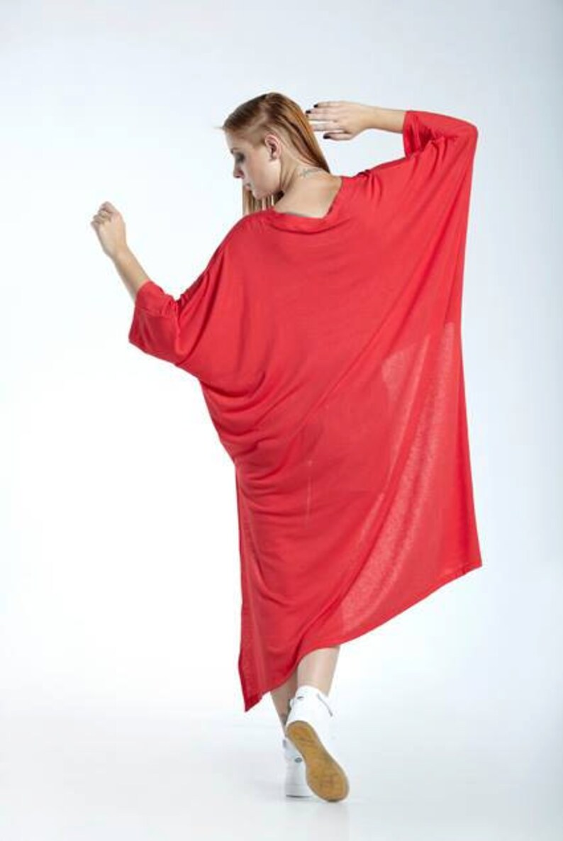May include: A loose-fitting, vibrant red dress featuring a wide, rounded neckline and long, flowing batwing sleeves. The garment has a relaxed, oversized silhouette that drapes down to the lower calf, paired with white athletic sneakers.