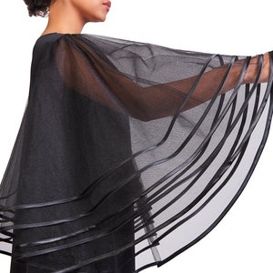 May include: A black sheer capelet featuring wide, flowing sleeves made of translucent mesh fabric. The hem of the capelet and the edges of the sleeves are finished with multiple horizontal bands of solid black ribbon trim, creating a layered effect.