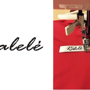 May include: A white fabric clothing label with the black text Ralel&eacute; printed in a cursive script font. The label is being sewn onto a piece of bright red fabric using a silver metal sewing machine presser foot and needle mechanism.