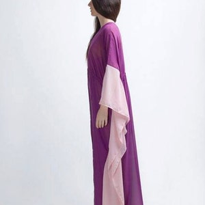 Puede incluir: Un vestido largo y fluido de color p&uacute;rpura con mangas anchas en un rosa claro contrastante. El vestido est&aacute; hecho de una tela transparente y tiene un ajuste holgado y c&oacute;modo. La persona lleva sandalias.