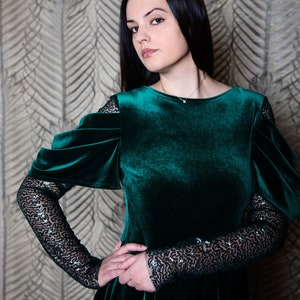 May include: A woman wearing a dark green velvet dress with black sequin sleeves. The dress has a round neckline and a fitted bodice.