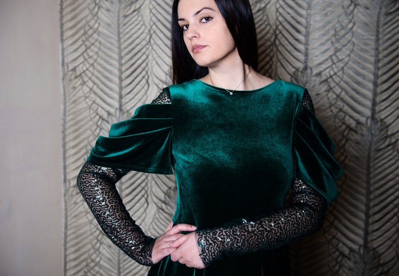 May include: A woman wearing a dark green velvet dress with black sequin sleeves. The dress has a round neckline and a fitted bodice.