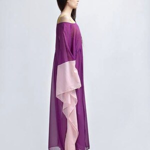 Puede incluir: Un vestido largo con hombros descubiertos en tonos morados y rosas. El vestido presenta un corpi&ntilde;o y mangas de color p&uacute;rpura oscuro, con un panel rosa en contraste en las mangas. El vestido es largo hasta el suelo y parece estar hecho de una tela ligera.