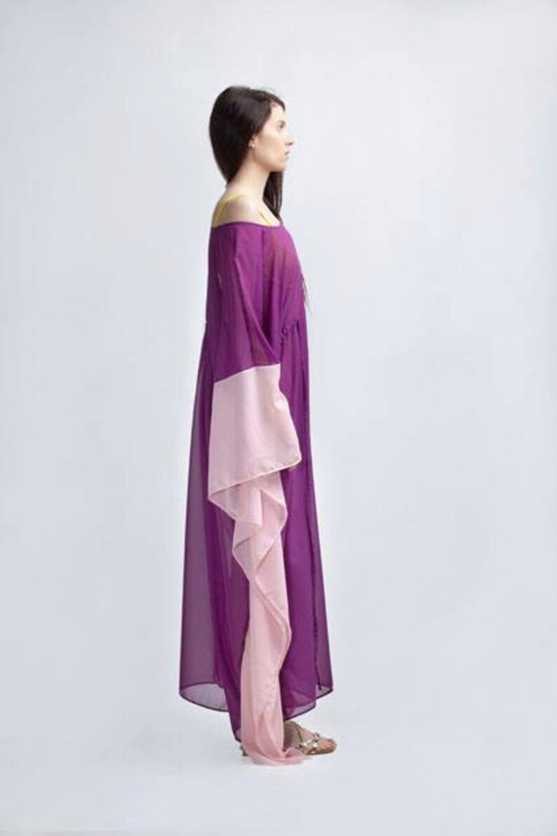 Puede incluir: Un vestido largo con hombros descubiertos en tonos morados y rosas. El vestido presenta un corpi&ntilde;o y mangas de color p&uacute;rpura oscuro, con un panel rosa en contraste en las mangas. El vestido es largo hasta el suelo y parece estar hecho de una tela ligera.