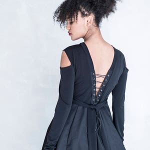 Pu&ograve; includere: Un abito nero a maniche lunghe con aperture sulle spalle e un profondo scollo a V sulla schiena. Il corpetto posteriore presenta un dettaglio stringato con occhielli in metallo argentato e un laccio in tessuto nero in vita, creando una gonna arricciata.