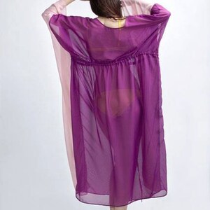May include: A sheer, loose-fitting kaftan featuring a vibrant purple center panel and contrasting pale pink side panels. The garment has a gathered waistline with a drawstring detail, wide sleeves, and a flowing, knee-length silhouette.