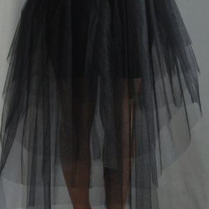 May include: A black tulle skirt featuring a high-low hemline with multiple layers of sheer fabric and a solid black waistband. The skirt is paired with red high-heeled shoes, creating a distinct contrast between the dark skirt and the bright footwear.