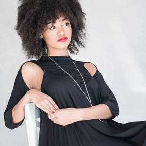 May include: A black dress with three-quarter length sleeves featuring shoulder cutouts and a high neckline. The garment is paired with a long, thin silver chain necklace that hangs down the front of the bodice, creating a simple and clean look.