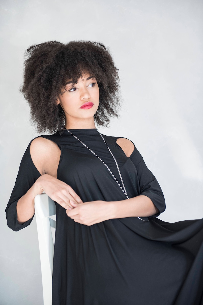 May include: A black dress with three-quarter length sleeves featuring shoulder cutouts and a high neckline. The garment is paired with a long, thin silver chain necklace that hangs down the front of the bodice, creating a simple and clean look.