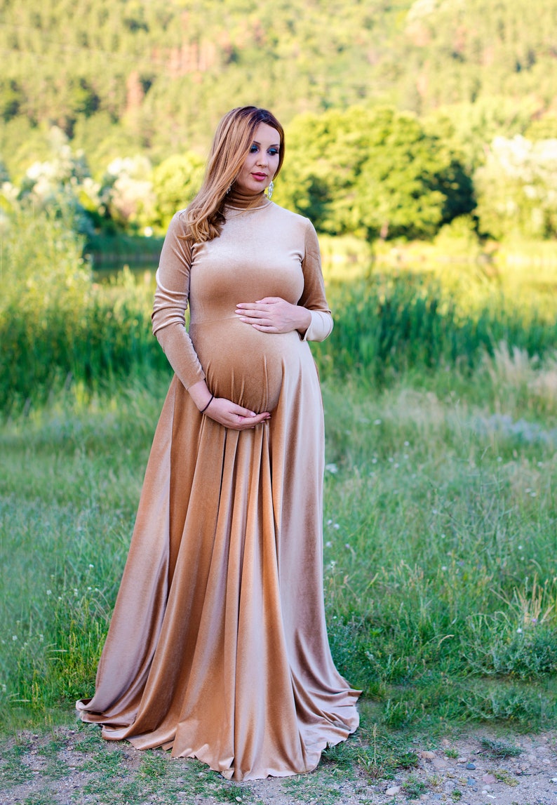 May include: A floor-length, long-sleeved velvet dress in a light tan or champagne color. The garment features a high mock-neck collar and a fitted bodice that transitions into a full, flowing skirt that reaches the ground, made of soft fabric.
