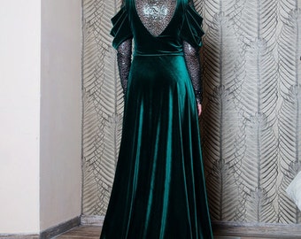 May include: A floor-length emerald green velvet gown featuring long sleeves with black sequined fabric, a V-shaped back panel with matching black sequins, and gathered shoulder details. The dress has a full skirt that extends into a train.
