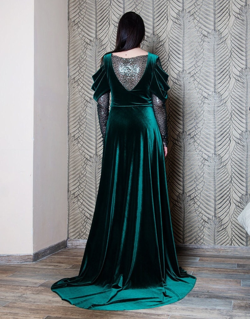 May include: A long, emerald green velvet dress with a low back and long sleeves. The sleeves are sheer and have a sparkly design. The dress has a flowing skirt.