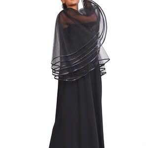 May include: A floor-length black dress featuring a sheer, layered tulle capelet overlay. The capelet is constructed from multiple tiers of black mesh fabric, each finished with a solid black ribbon trim along the curved edges, creating a voluminous silhouette.