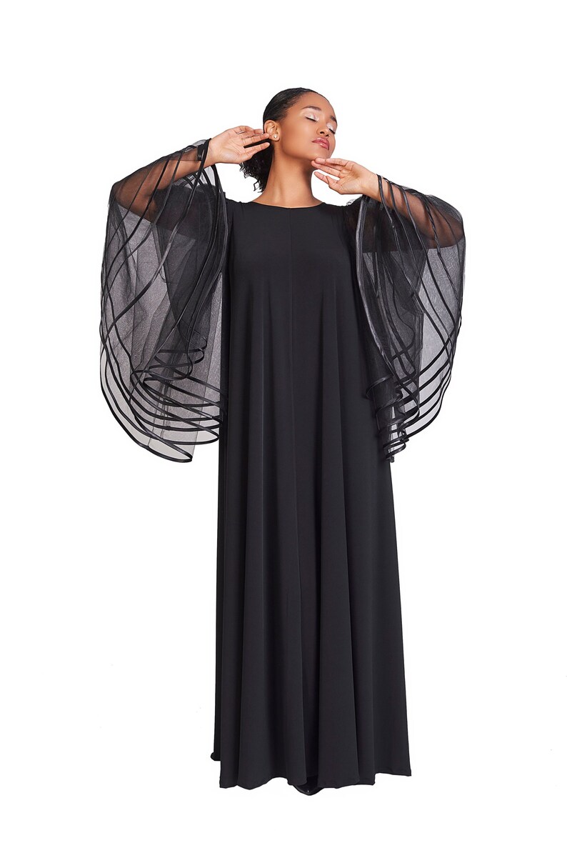 May include: A floor-length black dress featuring a round neckline and dramatic, wide, sheer sleeves. The sleeves are constructed from layers of black tulle or organza, accented with horizontal black ribbon trim that creates a structured, tiered effect.