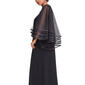 May include: A floor-length black dress featuring sheer, layered tulle sleeves. The sleeves are constructed with multiple tiers of black mesh fabric, each finished with a solid black ribbon trim along the edges, creating a voluminous, flowing silhouette.