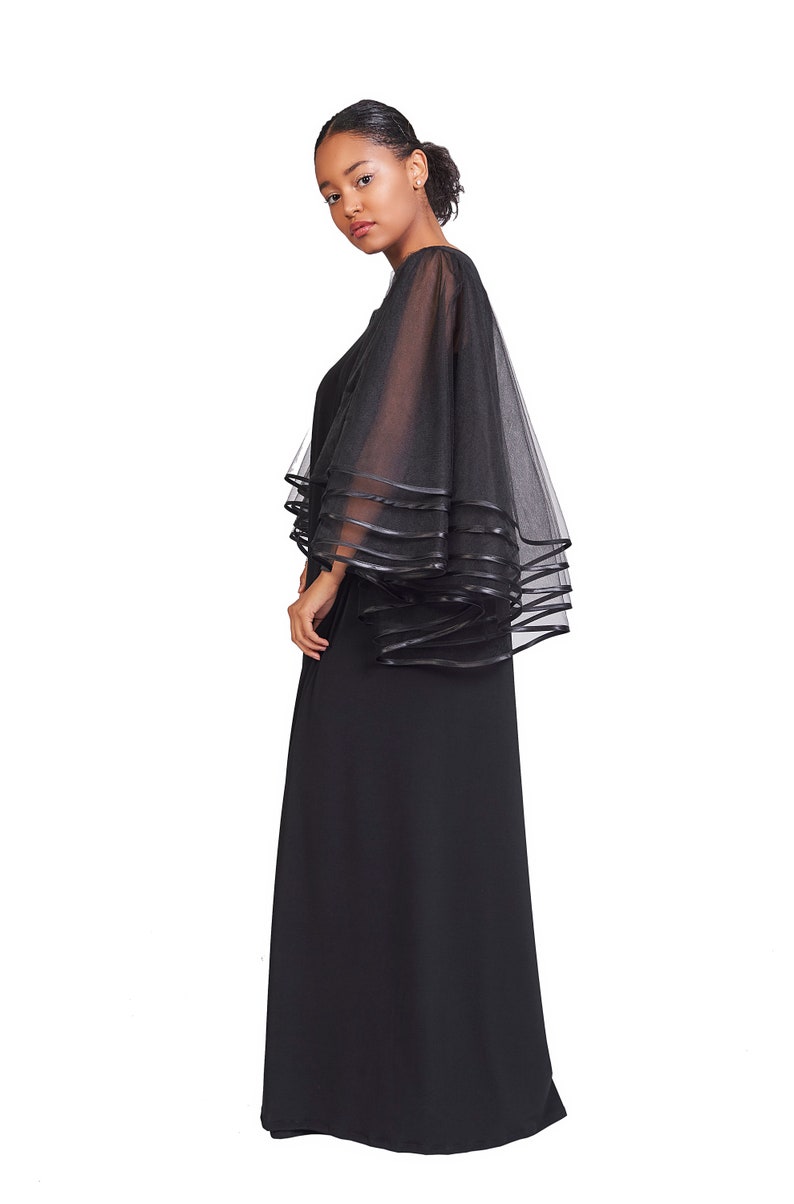 May include: A floor-length black dress featuring sheer, layered tulle sleeves. The sleeves are constructed with multiple tiers of black mesh fabric, each finished with a solid black ribbon trim along the edges, creating a voluminous, flowing silhouette.
