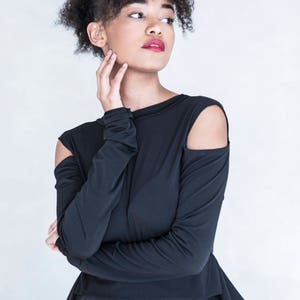 Pu&ograve; includere: Un top nero a maniche lunghe con spalle scoperte e scollo alto. Il capo presenta un corpetto aderente che si trasforma in una gonna svasata e plissettata in vita, creando una silhouette strutturata dalle linee pulite ed essenziali.