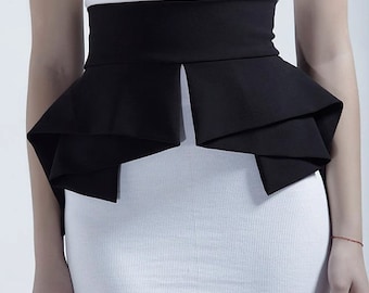 May include: A white ribbed sleeveless dress featuring a wide black waist belt with a structured peplum design. The belt has a smooth matte finish and layered fabric folds that extend outward from the waistline, creating a distinct silhouette.