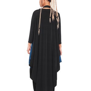 May include: A black long-sleeved tunic with a blue under layer. The tunic has a flowing, asymmetrical hemline. The model is wearing the tunic with their back to the camera.