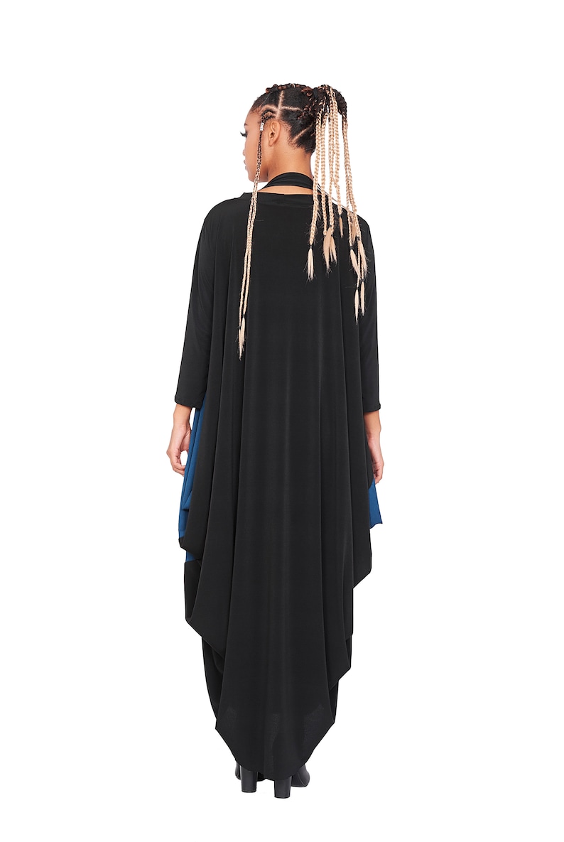 May include: A black long-sleeved tunic with a blue under layer. The tunic has a flowing, asymmetrical hemline. The model is wearing the tunic with their back to the camera.