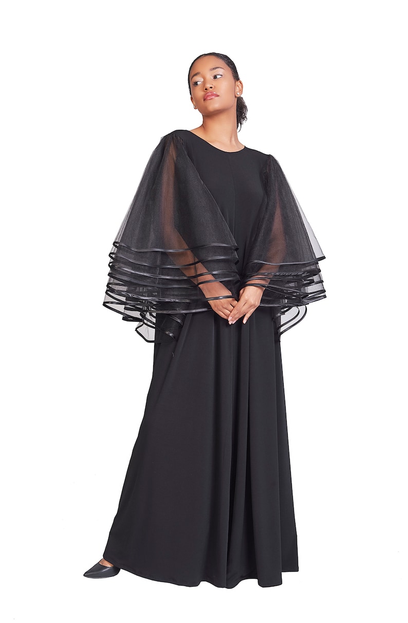 May include: A black maxi dress with a layered tulle cape. The dress has a round neckline and long sleeves. The cape is sheer and has a satin trim.