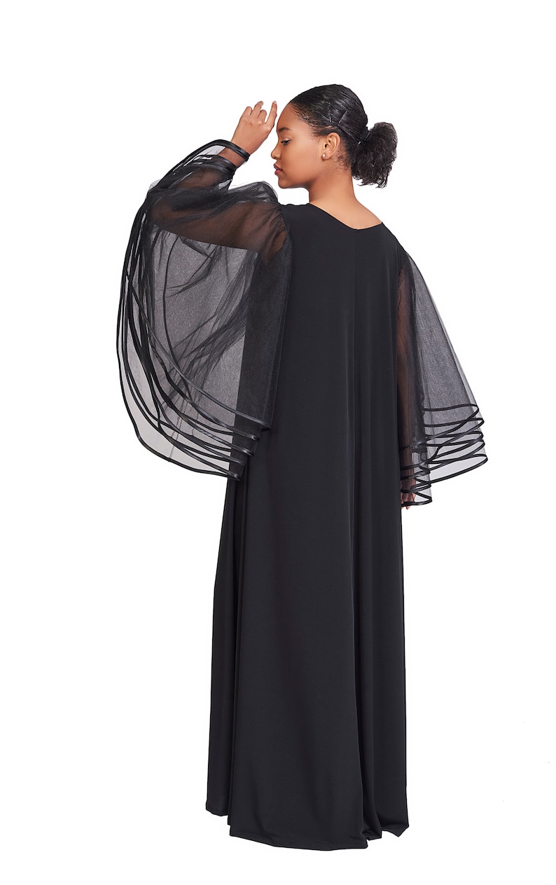 May include: A floor-length black dress featuring sheer, voluminous bell sleeves made of layered tulle fabric. The sleeves are accented with multiple horizontal bands of black trim at the cuffs, creating a tiered effect on this solid black garment.