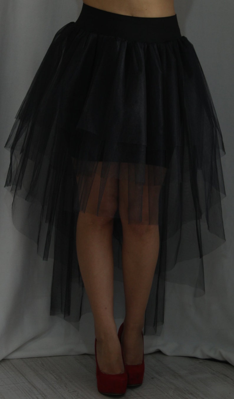 May include: A black tulle skirt with a high-low hemline. The skirt is layered and has a fitted waistband. The skirt is being worn with red high heels.