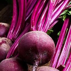 May include: Three red beets with their green leafy tops, arranged on a wooden surface.